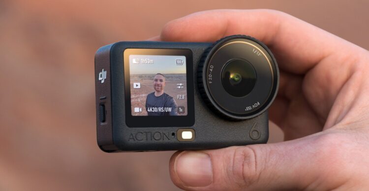 یک دوربین اکشن DJI Osmo Action 6 در دست، که صفحه نمایش جلویی آن یک سلفی از کاربر در محیط بیرون را نمایش می‌دهد.