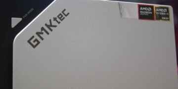 نمای نزدیک از یک مینی کامپیوتر یا کیس رومیزی نقره‌ای GMKtec با آرم‌های AMD Radeon Graphics و AMD Ryzen AI MAX+ در بالا سمت راست.