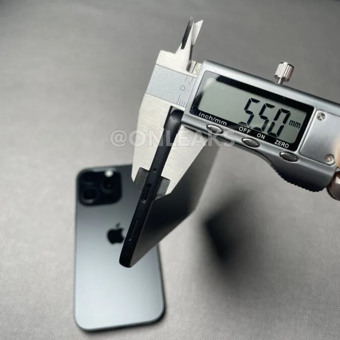 نمای جانبی یک گوشی مشکی رنگ که ضخامت آن با کولیس دیجیتال اندازهگیری شده و عدد ۵.۵۰ میلیمتر نمایش داده میشود و لوگوی اپل در پشت گوشی تار دیده میشود.