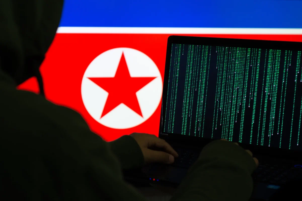 نمایی از فردی که با لپتاپاش دارد کد نویسی میکند و در پسزمینه پرچم آمریکای شمالی قرار گرفته