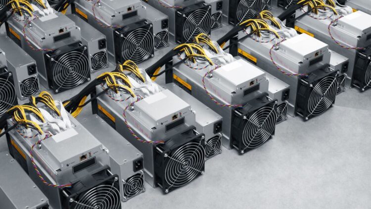 ردیف‌هایی از دستگاه‌های ماینینگ بیت‌کوین (Bitcoin miners) Bitmain Antminer با سیم‌کشی‌های زرد و سیاه که به صورت فشرده روی یک سطح خاکستری چیده شده‌اند.