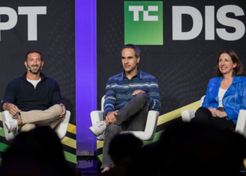 سه سخنران روی صندلیها در یک پنل گفتگو در کنفرانس TechCrunch Disrupt، که در پسزمینه یک بنر با لوگوی "DISRUPT" دیده میشود.