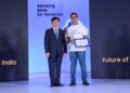 یک مرد کره‌ای با کت و شلوار در حال دادن گواهی یا جایزه به یک دانشجوی هندی که تی‌شرت آبی پوشیده، در مراسم "Samsung Solve for Tomorrow".