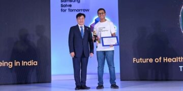یک مرد کرهای با کت و شلوار در حال دادن گواهی یا جایزه به یک دانشجوی هندی که تیشرت آبی پوشیده، در مراسم "Samsung Solve for Tomorrow".