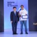 یک مرد کره‌ای با کت و شلوار در حال دادن گواهی یا جایزه به یک دانشجوی هندی که تی‌شرت آبی پوشیده، در مراسم "Samsung Solve for Tomorrow".