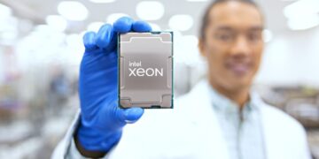 یک مرد با دستکش آبی در حال نگه داشتن تراشه Intel Xeon (احتمالاً Granite Rapids) با روپوش سفید در یک آزمایشگاه.