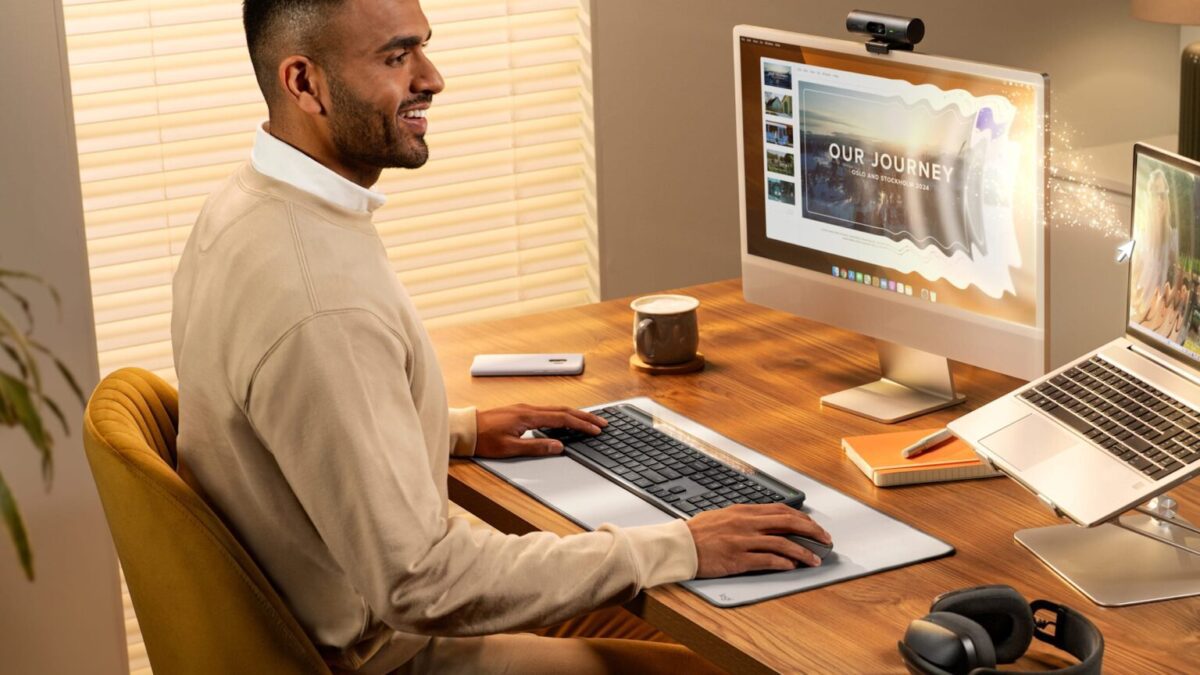 یک مرد در حال استفاده از کیبورد Logitech Signature Slim Solar+ K980 و ماوس بی‌سیم روی یک پد میز بزرگ، در حال کار با یک کامپیوتر رومیزی و لپ‌تاپ.