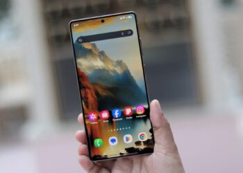 یک دست گوشی هوشمند سامسونگ با صفحه‌نمایش روشن و والپیپر کوهستانی را نگه داشته است.