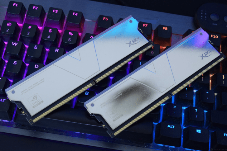 دو ماژول حافظه RAM به رنگ نقرهای و سفید با نورپردازی RGB در بالای آنها، که روی یک صفحه کلید مکانیکی با نورپردازی آبی و بنفش قرار گرفتهاند.