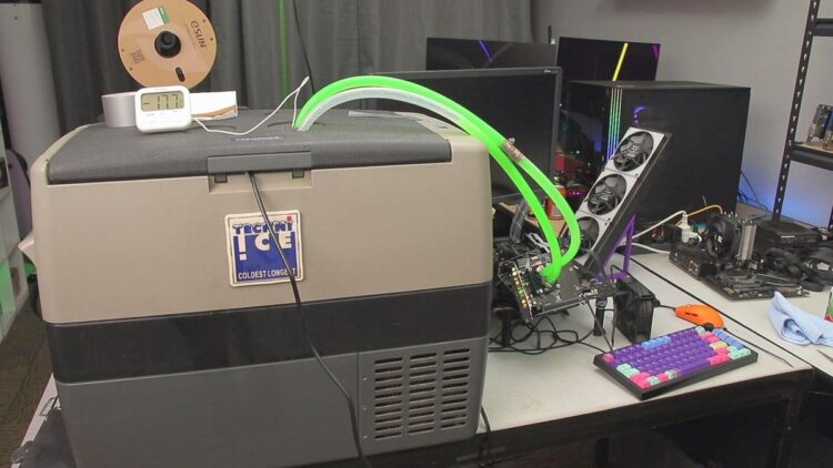 کارت گرافیک NVIDIA RTX 5050 که به یک بلوک خنک‌کننده آب متصل شده است و لوله‌های سبز فلورسنت مایع خنک‌کننده از آن به یک فریزر کمپینگ Tecni Ice متصل شده‌اند، در یک محیط دسکتاپ.