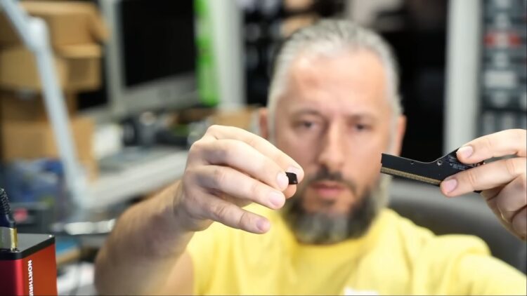 یک مرد ریشو که قطعه شکسته یک کانکتور کارت گرافیک را در یک دست و بخش اصلی کانکتور را در دست دیگر گرفته است.