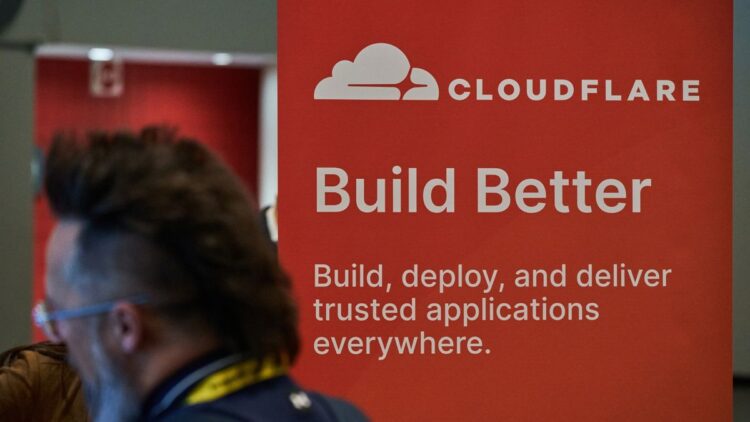 یک بنر تبلیغاتی Cloudflare با لوگوی سفید و شعار "Build Better" که در یک رویداد یا کنفرانس دیده می‌شود.