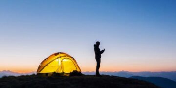 تصویری از یک فرد که کنار چادر کمپ‌اش در محلی بدون تکنولوژی دارد از گوشی استفاده می‌کند