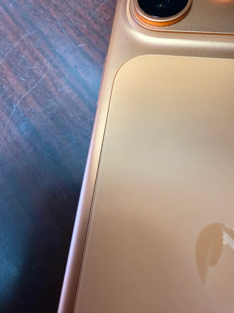 مقایسه دو عکس نزدیک از قسمت بالای پشتی یک iPhone 17 (نقره‌ای) که نشان‌دهنده یک مشکل کنترل کیفیت احتمالی (QC) یا عدم هم‌ترازی در پنل شیشه‌ای پشتی آن در نزدیکی دکمه‌های کناری است.