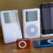 مجموعه‌ای از مدل‌های مختلف iPod و آیفون قدیمی (از جمله Classic، Mini، Nano و دو مدل آیفون) که روی یک سطح چوبی در کنار هم قرار گرفته‌اند.