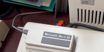نمای نزدیک از دستگاه خارجی "Microsoft Mach 10" با کابل‌های متصل، که در کنار یک واحد کامپیوتر قدیمی IBM Personal Computer XT قرار دارد.