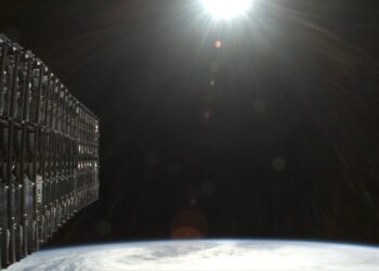 نمای نزدیک از مجموعه ماهوارههای Starlink متصلبههم در مدار پایین زمین، با پسزمینه انحنای زمین و تابش نور خورشید، نماد توسعه اینترنت ماهوارهای اسپیسایکس