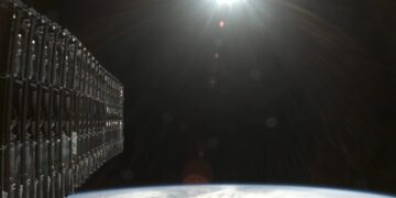 نمای نزدیک از مجموعه ماهوارههای Starlink متصلبههم در مدار پایین زمین، با پسزمینه انحنای زمین و تابش نور خورشید، نماد توسعه اینترنت ماهوارهای اسپیسایکس