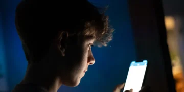 نمای جانبی گوشی هوشمند در محیط کم‌نور با صفحه‌نمایش روشن، نمایش محتوای اپلیکیشن در دست کاربر و نور صفحه به‌عنوان منبع نور اصلی صحنه