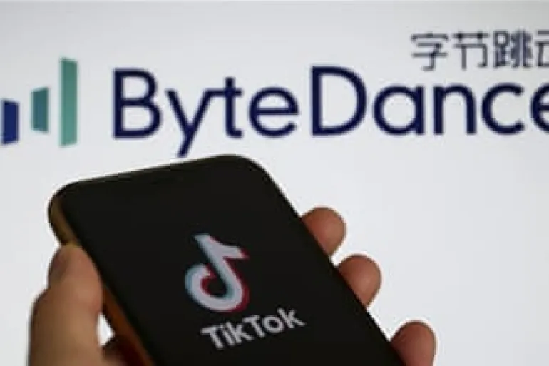 دستی که گوشی با لوگوی TikTok را نگه داشته و لوگوی شرکت ByteDance در پس‌زمینه محو دیده می‌شود.