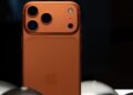نمای نزدیک به پشت یک گوشی نارنجی رنگ (ظاهراً iPhone 17 Pro) با سه لنز دوربین بزرگ.