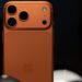 نمای نزدیک به پشت یک گوشی نارنجی رنگ (ظاهراً iPhone 17 Pro) با سه لنز دوربین بزرگ.