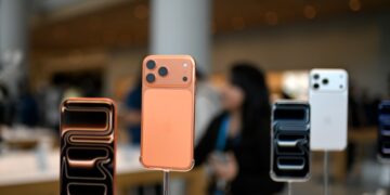 نمای نزدیک از ماکت‌های پشت و جلوی آیفون‌های جدید با رنگ‌های نارنجی و سفید در فروشگاه.