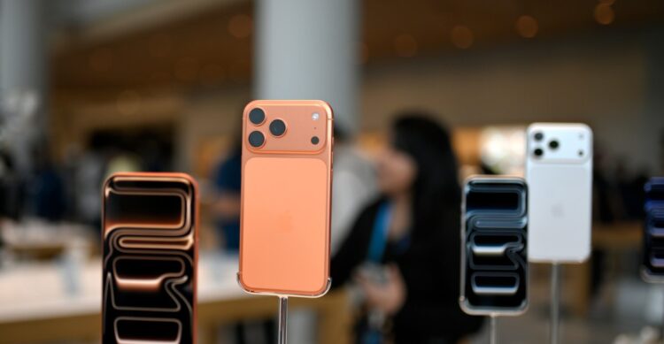 نمای نزدیک از ماکت‌های پشت و جلوی آیفون‌های جدید با رنگ‌های نارنجی و سفید در فروشگاه.