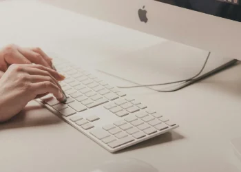 دست‌های کاربر در حال تایپ روی کیبورد مک‌بوک یا آی‌مک اپل در محیط روشن، نمادین از فعالیت‌های مرتبط با امنیت سایبری و حملات فیشینگ