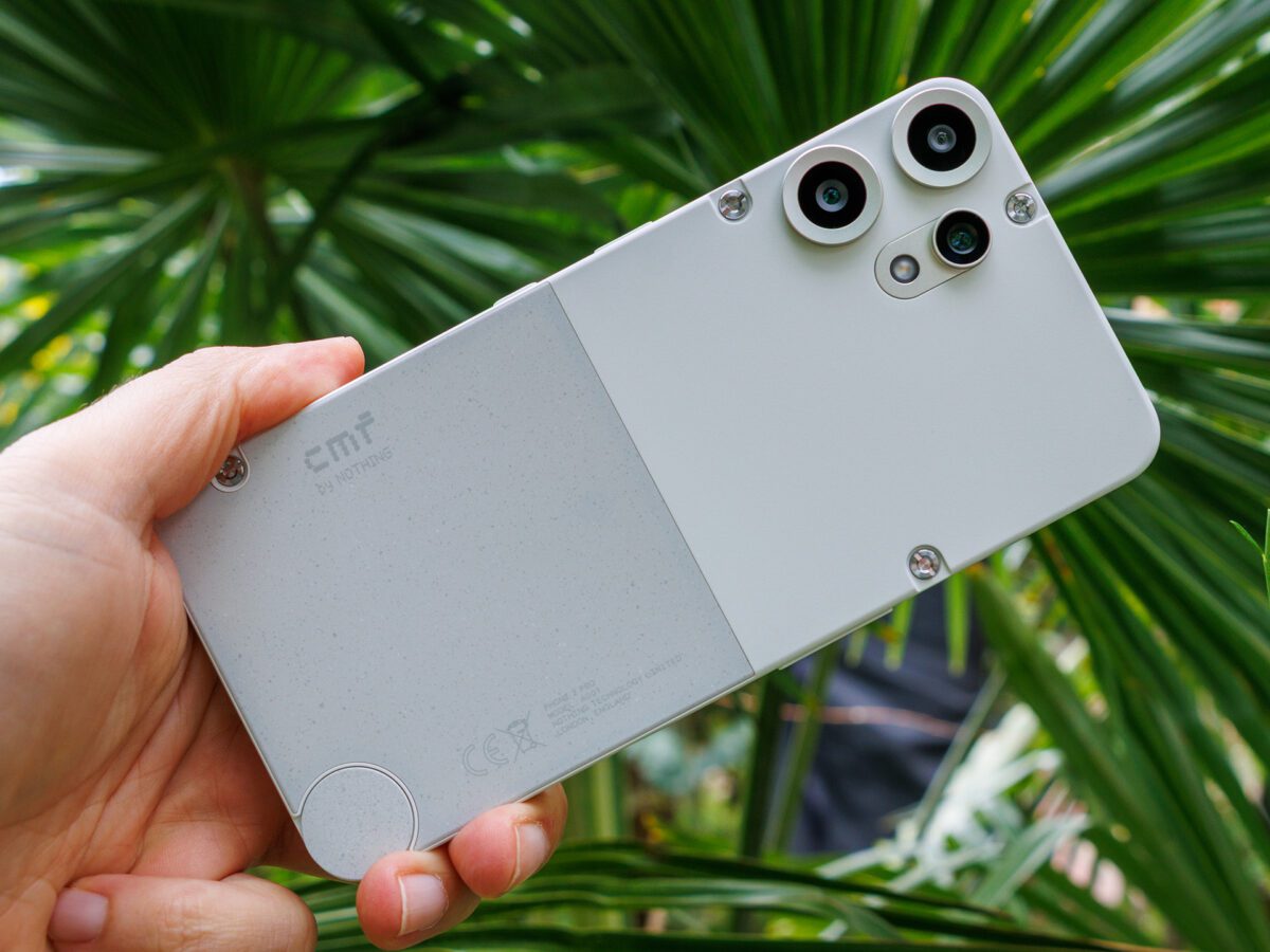 نمای نزدیک از پشت گوشی CMF Phone 2 Pro در دست، با رنگ سفید مایل به خاکستری و پیچ‌های طراحی ماژولار.