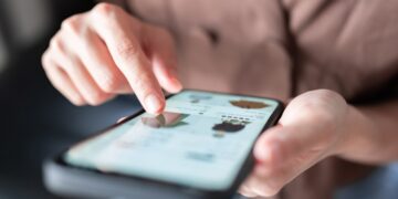 نمای نزدیک از دستان کاربر در حال کار با اپلیکیشن خرید آنلاین لباس روی گوشی هوشمند.