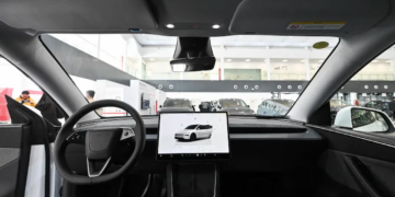 نمای داخلی کابین خودروی تسلا شامل فرمان و صفحه نمایشگر لمسی مرکزی در محیط نمایشگاه.