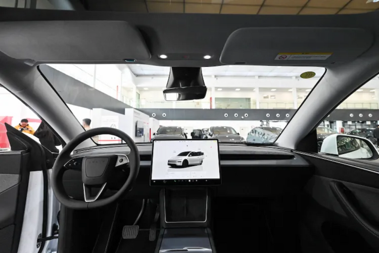 نمای داخلی کابین خودروی تسلا شامل فرمان و صفحه نمایشگر لمسی مرکزی در محیط نمایشگاه.