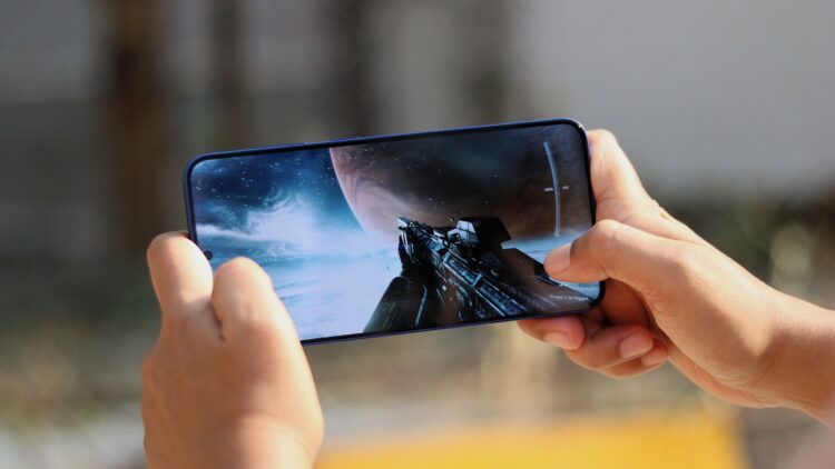 نمای نزدیک از دستهای شخصی که با گوشی هوشمند یک بازی ویدیویی فضایی را اجرا میکند.