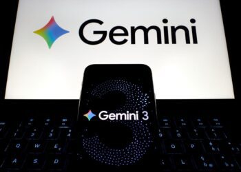 یک گوشی هوشمند با صفحه «Gemini 3» که روی کیبورد لپ‌تاپ قرار گرفته و لوگوی گوگل جمنای در نمایشگر پشت آن دیده می‌شود.