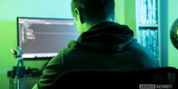 تصویر نمادین از یک هکر با هودی که در اتاقی با نور سبز جلوی کامپیوتر نشسته است.
