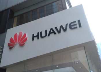 نمای بیرونی ساختمان هوآوی با لوگوی قرمز Huawei و تابلو سفیدرنگ در نمای شهری مدرن، نشان‌دهنده هویت برند و دفتر رسمی شرکت هوآوی در حوزه فناوری و ارتباطات