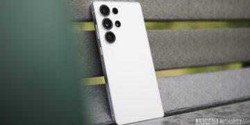 نمای نزدیک از پشت یک گوشی هوشمند سفید رنگ سری سامسونگ گلکسی S (احتمالاً S26 Ultra) که به یک سطح نیمکتی خاکستری متمایل شده و سیستم دوربین آن مشخص است.