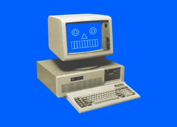 کامپیوتر قدیمی رومیزی با مانیتور CRT و صفحه‌نمایشی شامل شکل‌های هندسی شبیه صورت کارتونی روی پس‌زمینه آبی یکدست