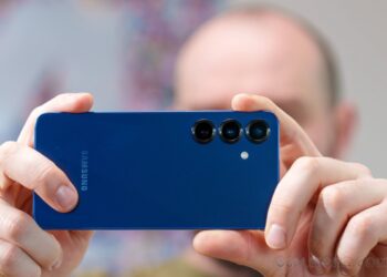 شخصی در حال عکاسی با یک گوشی سامسونگ گلکسی آبی رنگ که لنزهای سه‌گانه دوربین پشت آن مشخص است.