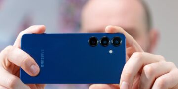 شخصی در حال عکاسی با یک گوشی سامسونگ گلکسی آبی رنگ که لنزهای سهگانه دوربین پشت آن مشخص است.