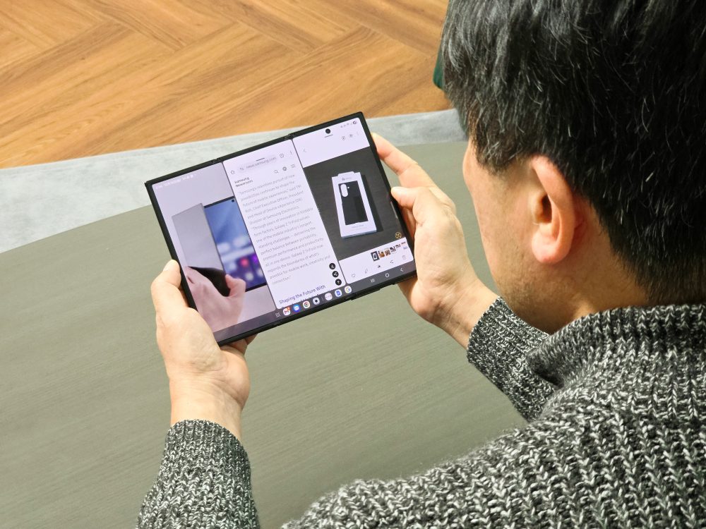 نمای از پشت سر فردی که یک گوشی تاشو بزرگ (شبیه تبلت) سامسونگ را با هر دو دست گرفته و در حال مطالعه متن روی آن است.