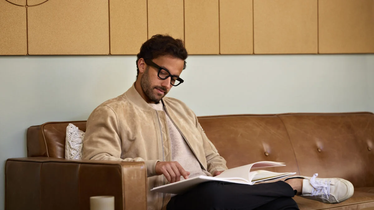 فردی در حال نشستن روی مبل و مطالعه کتاب در فضای داخلی روشن و مینیمال