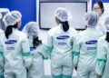 صفی از کارکنان یا بازدیدکنندگان با لباس‌های محافظ مخصوص (Cleanroom suit) و لوگوی سامسونگ.