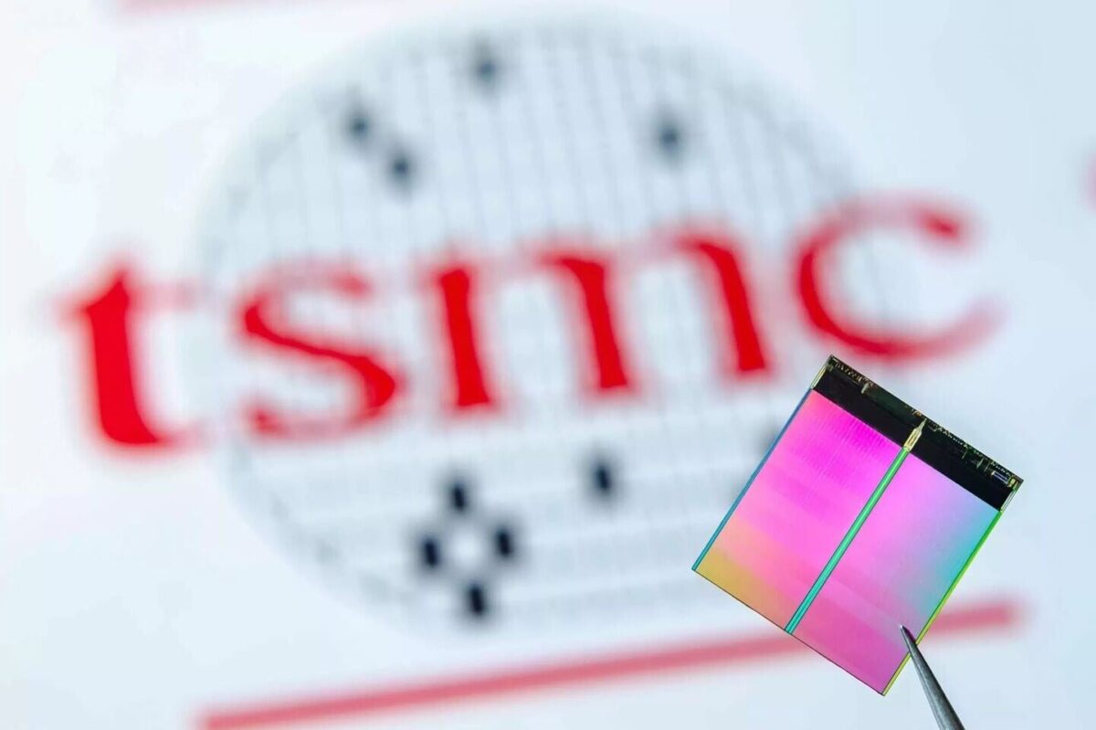 یک ریزتراشه (Chip) که با پنس نگه داشته شده و لوگوی شرکت TSMC در پسزمینه آن به صورت تار دیده میشود.