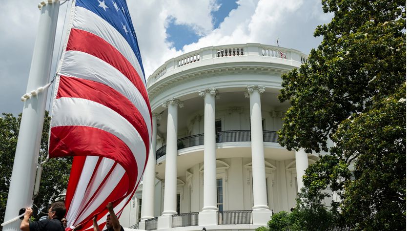 نمای عمارت کاخ سفید در واشینگتن در حالی که پرچم بزرگ ایالات متحده در جلوی کادر قرار دارد.