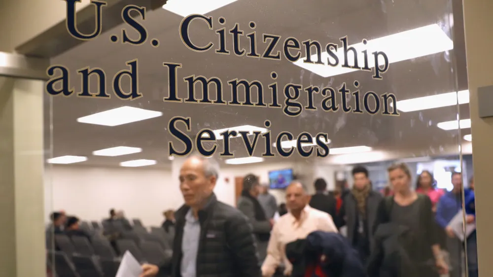 درب شیشهای با نوشته طلایی «خدمات شهروندی و مهاجرت ایالات متحده» و مراجعین در پسزمینه.