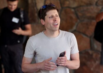 سم آلتمن (Sam Altman) در فضای باز در حالی که یک گوشی هوشمند در دست دارد و به روبرو نگاه می‌کند.