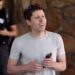 سم آلتمن (Sam Altman) در فضای باز در حالی که یک گوشی هوشمند در دست دارد و به روبرو نگاه می‌کند.