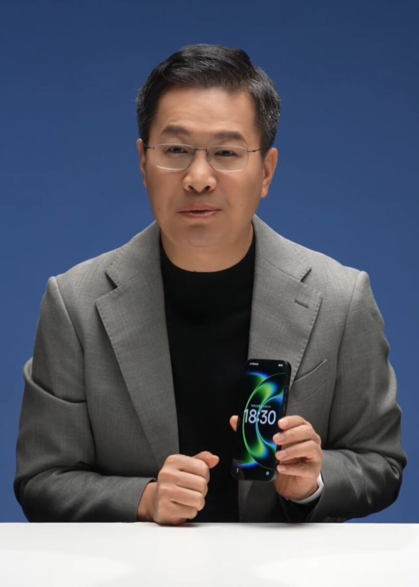 مردی با کت خاکستری که گوشی شیائومی را برای نمایش نمایشگر و طراحی آن در دست گرفته است.